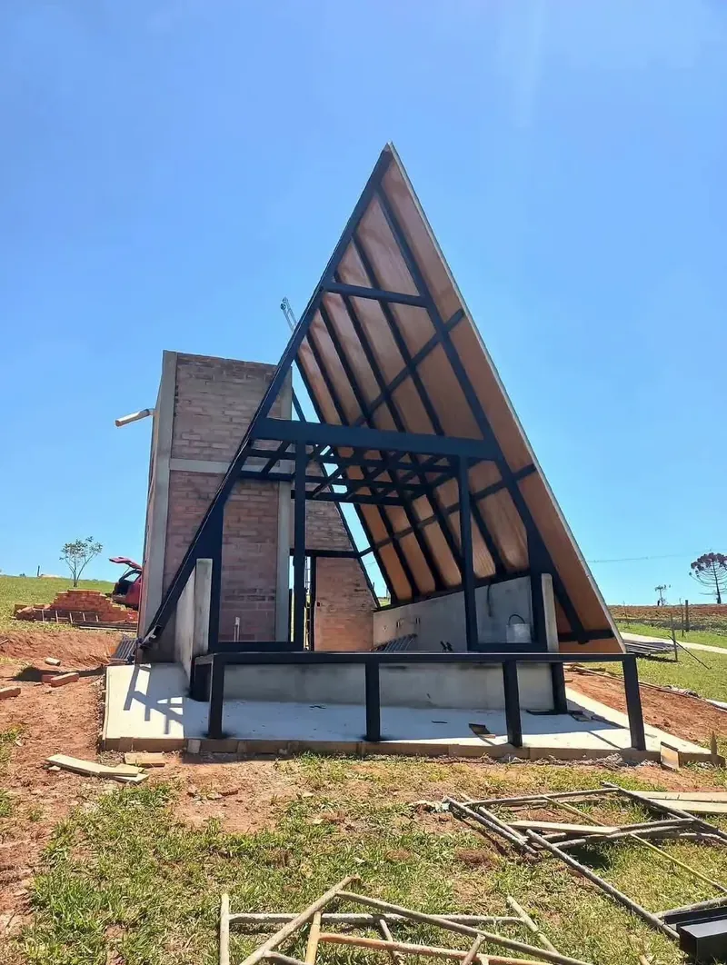 Cabaña en A de INTEGRA en obra: estructura de perfiles negros con paneles tipo madera bajo cielo azul