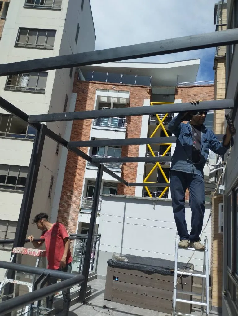 Trabajadores instalando las vigas de una pérgola metálica en la terraza de un edificio