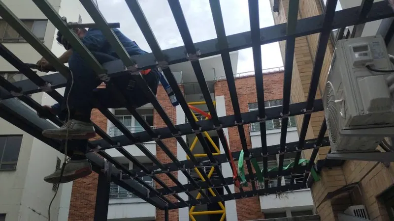 Soldador trabajando sobre la retícula metálica de una pérgola en la terraza de un edificio
