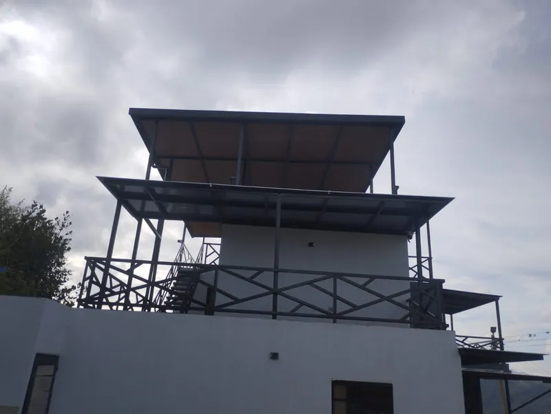 Casa blanca con terrazas, barandas en X y cubiertas metálicas escalonadas bajo cielo nublado