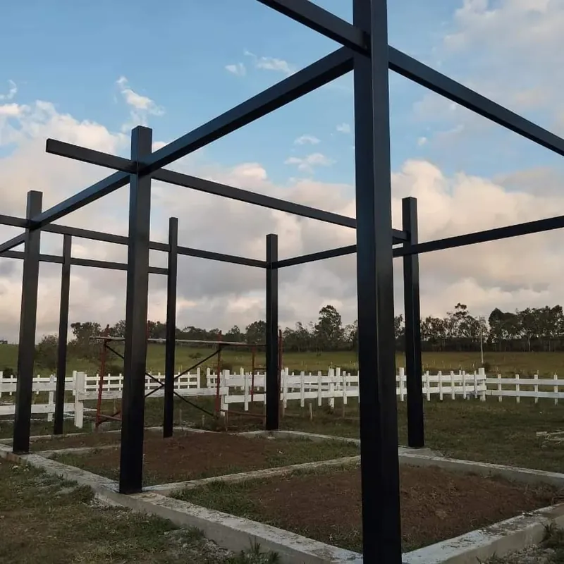 Estructura metálica negra de columnas y vigas sobre bases de concreto en un lote con cerca blanca