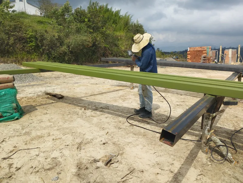 Trabajador con sombrero soldando una viga verde apoyada sobre perfiles en el terreno