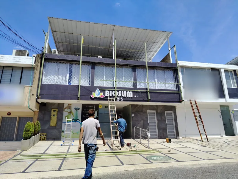 Frente del local comercial con la nueva estructura metálica y la cubierta instaladas sobre la fachada, con trabajadores en la acera
