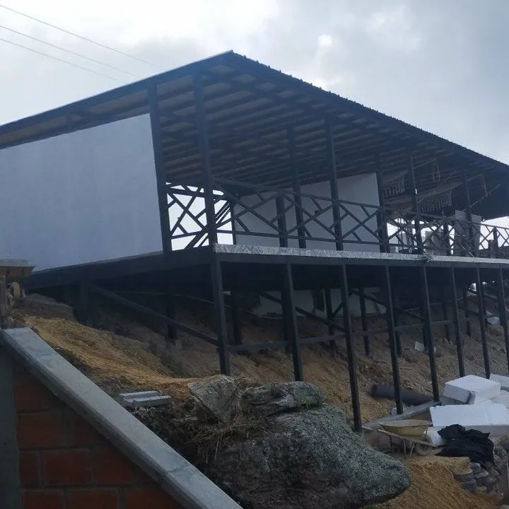 Casa elevada sobre columnas metálicas en un terreno inclinado, con baranda en X