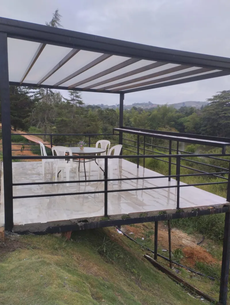 Terraza en voladizo con estructura metálica, cubierta traslúcida y baranda, sobre una ladera con vista a las montañas