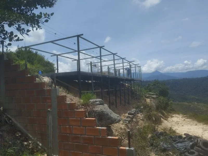 Estructura metálica sobre una ladera con muro de ladrillo y montañas al fondo