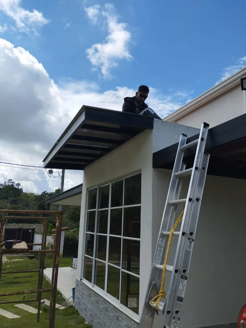 Trabajador sobre la pérgola instalando la cubierta junto al ventanal de la casa
