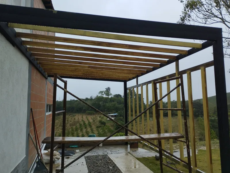 Pérgola metálica con listones de madera en el techo y en el costado, con andamio durante la obra