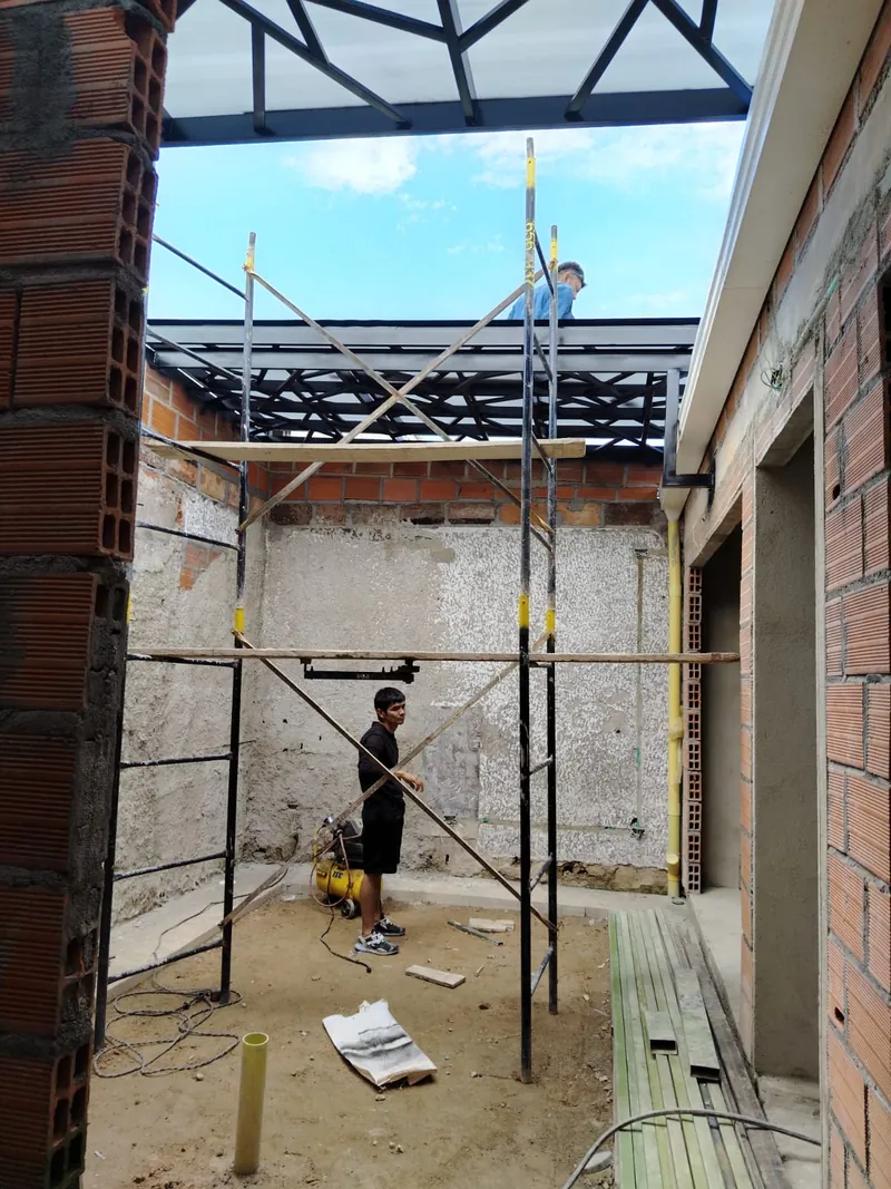Patio en obra con andamios bajo la retícula geométrica de la pérgola