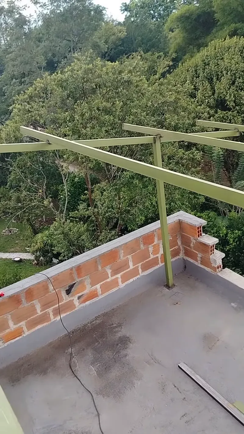 Perfiles metálicos con anticorrosivo sobre el muro de ladrillo de una azotea rodeada de árboles