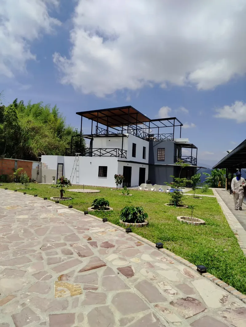 Casa blanca de tres pisos con la pérgola metálica y el techo tipo madera que INTEGRA construyó en la azotea, vista desde el camino de piedra del jardín