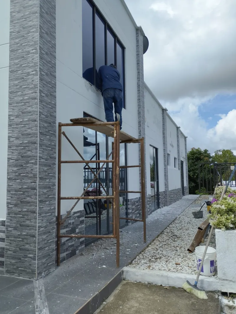 Trabajador en andamio junto a la ventana de la casa durante la obra de la terraza