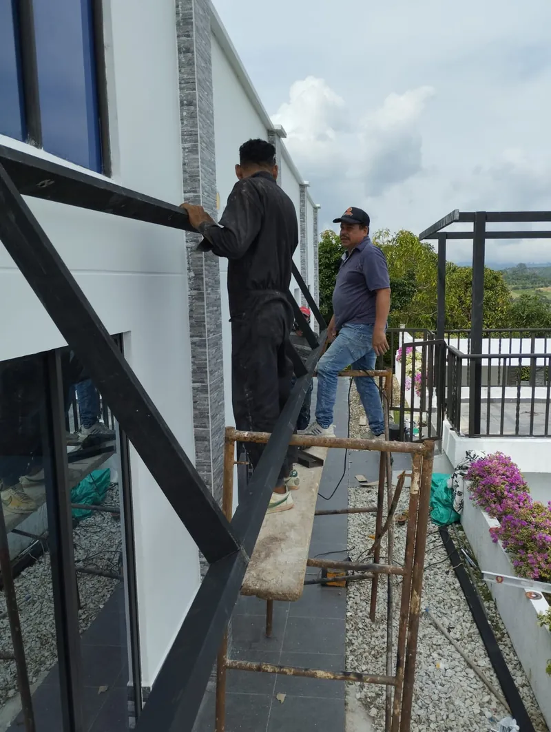 Dos trabajadores montando una viga metálica negra en la terraza de una casa con enchape de piedra