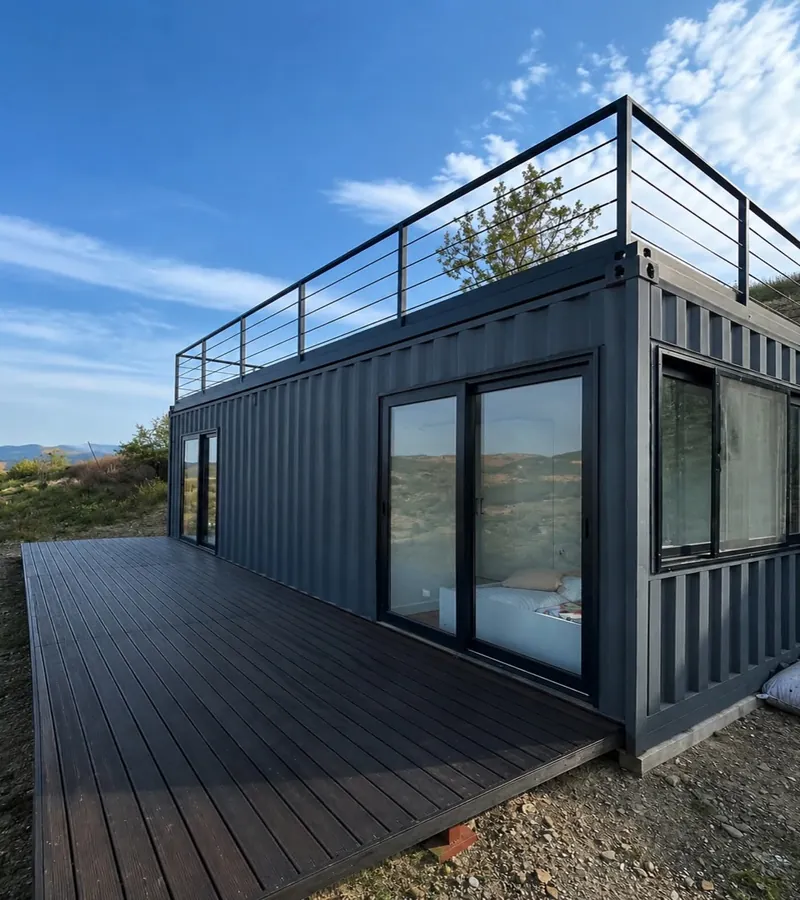 Imagen de referencia: vivienda en contenedor marítimo negro con listones de madera, deck y baranda en la cubierta